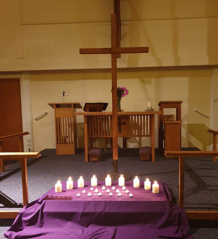 A visual focus of candles on a purple cloth in front of a large cross.