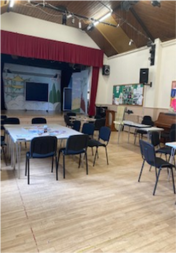 The inside of the church hall showing the stage and chairs around large tables.