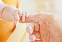 A baby's hand clasps a parent's finger.